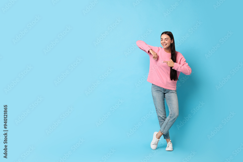 Smiling woman pointing at something on light blue background. Space for text Smiling woman pointing at something on light blue background. Space for text