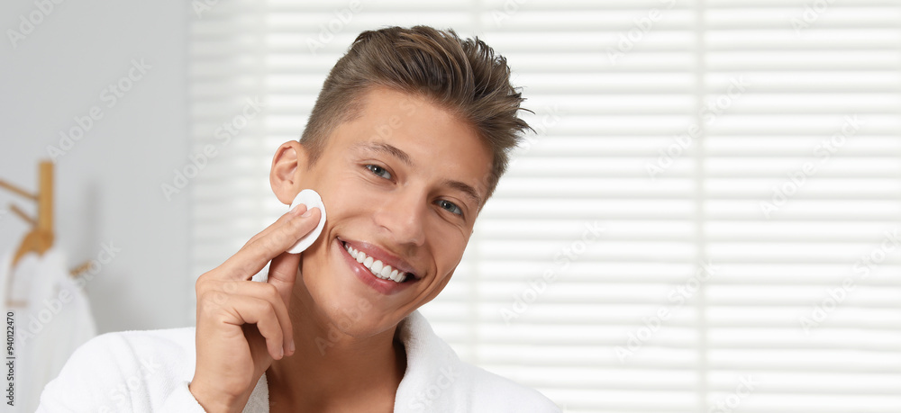 Handsome young man cleaning face with cotton pad in bathroom. Banner design with space for text Handsome young man cleaning face with cotton pad in bathroom. Banner design with space for text