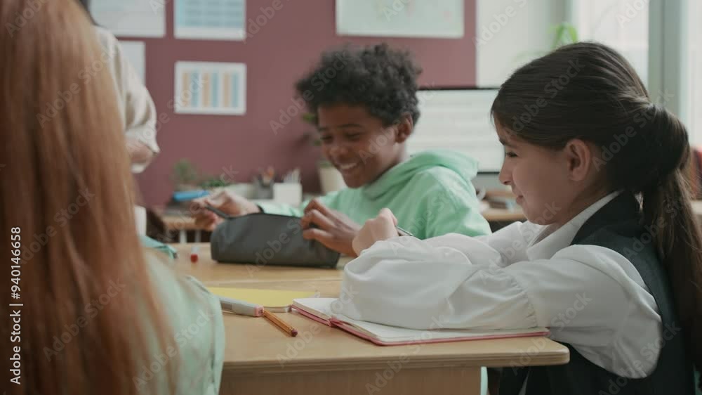 Medium shot of smiling, friendly 10-year-old African American boy sharing pens with Middle Eastern girl during lesson in language school, girl thanking him and writing Medium shot of smiling, friendly 10-year-old African American boy sharing pens with Middle Eastern girl during lesson in language school, girl thanking him and writing