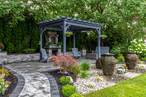 Large gray pergola on pavers with stone fireplace and waterfall urns for backyard oasis landscape design