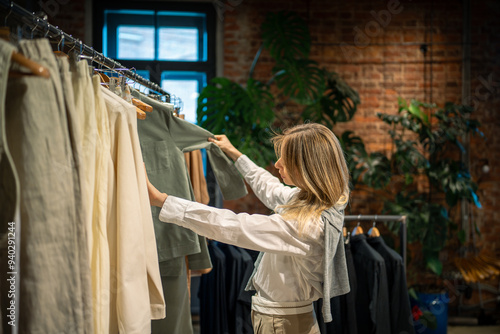 Quadro su tela Tranquil female buyer sorting, choosing clothes on rail in dress outlet