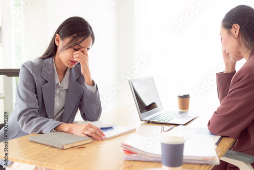 Asian woman pressing 2 hands on forehead feeling stressed, worried about bad financial business with documents and laptop on table