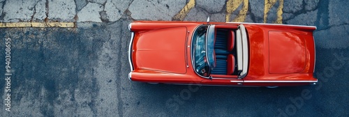 A classic red convertible car parked on a cracked asphalt road. The car is viewed from above, showcasing its sleek design and open top. It symbolizes freedom, adventure, classic style, and the nostalg photo