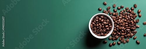 A white cup filled with roasted coffee beans sits on a green background, with some beans scattered around it. This image symbolizes energy, morning ritual, caffeine boost, and the aroma of freshly bre photo