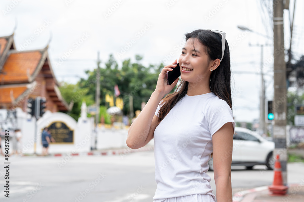 A beautiful Asian woman is talking on the phone while standing by the street in the city. A beautiful Asian woman is talking on the phone while standing by the street in the city.