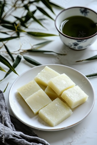 A plate of soft, white mochi squares and a cup of green tea on a marble surface.