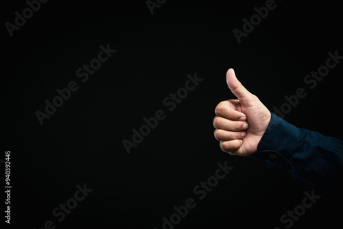 Hand showing thumbs up gesture, positive approval sign against dark background.