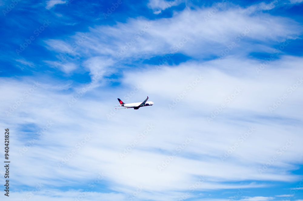 Fototapeta premium Airplane Flying High in a Clear Blue Sky with White Clouds