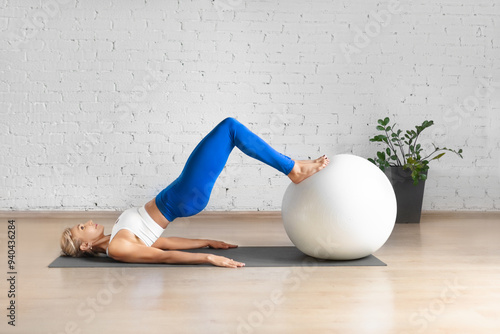 Workout with fitness ball. Fit Caucasian woman practice hamstring roll-in using props in loft studio indoor.