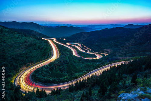At night, on the winding mountain road, the car lights form a long stream of light