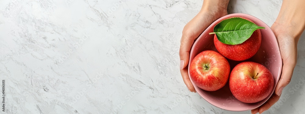 A person holds a bowl filled with apples One apple atop displays a green leaf A person holds a bowl filled with apples One apple atop displays a green leaf