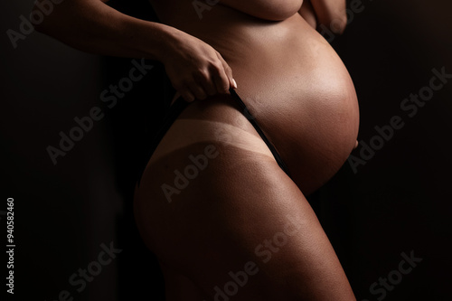 Pregnant woman pulls back her panties showing instant tan. Vertical photo. 