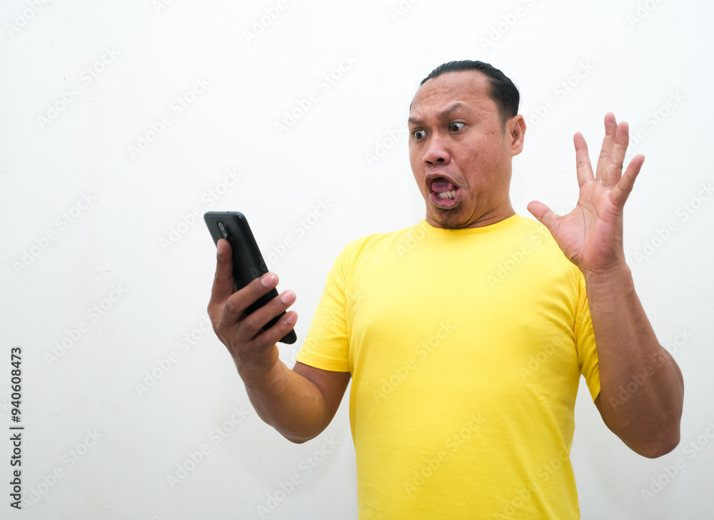 Young asian man wearing yellow t-shirts showing shocked expression while holding mobile phone Young asian man wearing yellow t-shirts showing shocked expression while holding mobile phone