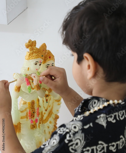 cute little indian boy is giving flute to lord Krishna and praying radhe krishna. he has wore Kurta with Radha name written in Hindi. he has devoted himseff in krishna bhakti  photo