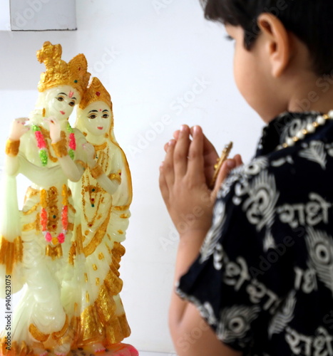 cute little indian boy is praying lord Krishna and radha. he has wore Kurta with Radha name written in Hindi. he is folding two hands and praying god.  photo