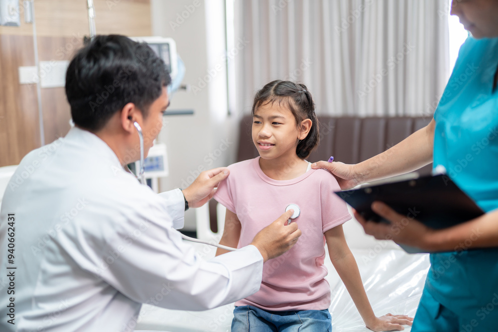 Obraz premium Asian male doctor and a female nurse gently examine a young girl in the hospital, ensuring her comfort and care throughout the process.