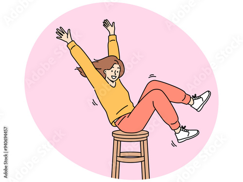 Happy girl is spinning on wooden chair, raising hands up and sharing good mood with others. Positive teenager girl in stylish clothes enjoys life without wanting to pay attention to troubles