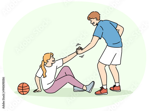 Basketball caviar helps fallen girl to stand up, showing team solidarity with injured opponent. Responsive friend lending helping hand to friend sitting on ground near basketball ball