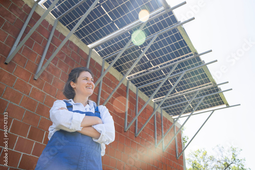 Happy engineer with arms crossed standing below solar panels at sunny day photo