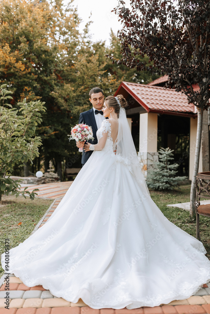 A bride and groom are standing in front of a red house with a white dress and a white veil A bride and groom are standing in front of a red house with a white dress and a white veil