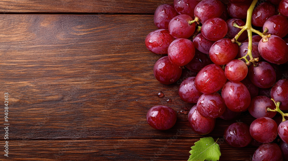 Fresh red grapes arranged on a rustic wooden surface with droplets of water, showcasing their lush texture and vibrant color Fresh red grapes arranged on a rustic wooden surface with droplets of water, showcasing their lush texture and vibrant color