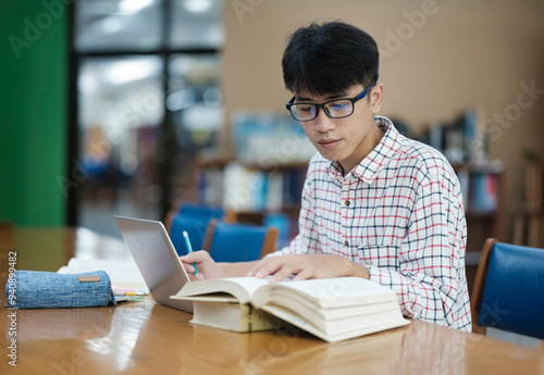 Young Asian male sitting inside a library alone doing research. Man working on a project. Young man doing research for a case.