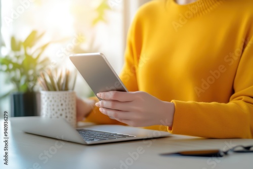 A person in a yellow sweater uses a smartphone while sitting at a desk, showcasing modern lifestyle and technology integration.