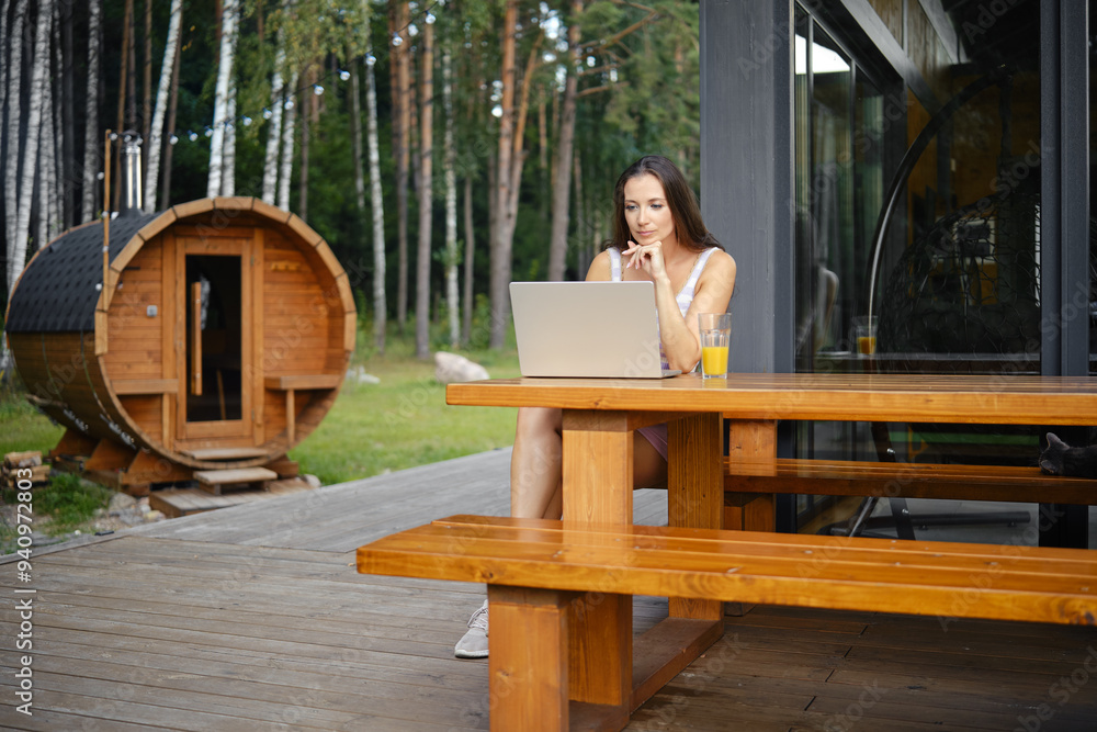 Woman watching movie on a laptop while sitting on a wooden bench on the terrace of a country house Woman watching movie on a laptop while sitting on a wooden bench on the terrace of a country house
