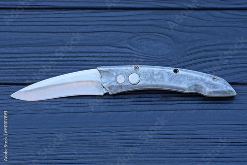 one gray metal folding knife lies on a black wooden table