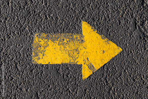 The yellow arrow is painted on the surface of the asphalt with a thick layer of paint. Top view.