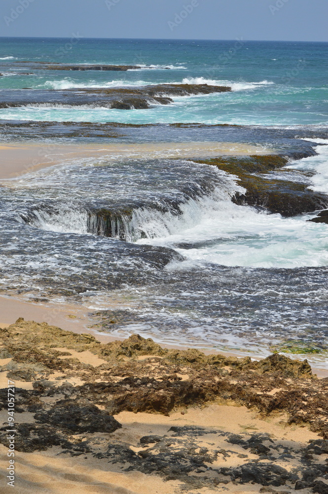 A scenic view of unique rock formations along a sandy beach at low tide, with gentle waves breaking in the background. The image captures the natural beauty and tranquility of the coastal landscape A scenic view of unique rock formations along a sandy beach at low tide, with gentle waves breaking in the background. The image captures the natural beauty and tranquility of the coastal landscape