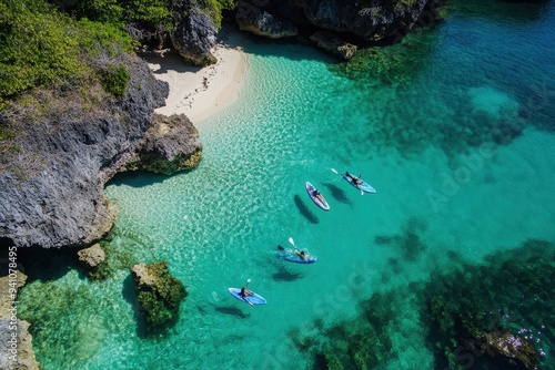 A group of people enjoys paddleboarding in the crystal-clear turquoise waters of a secluded beach surrounded by cliffs, highlighting the nature, fun, and adventure they engage in.