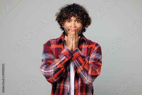 Young happy shocked surprised excited fun Indian man he wears red shirt casual clothes cover mouth with hand looking camera isolated on plain grey color background studio portrait. Lifestyle concept. photo