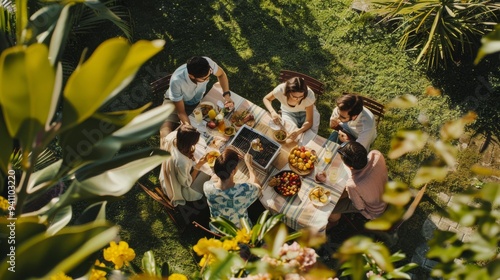 An aerial view of a joyous outdoor gathering where six friends enjoy a meal around a garden table adorned with fruits and drinks, surrounded by lush greenery.