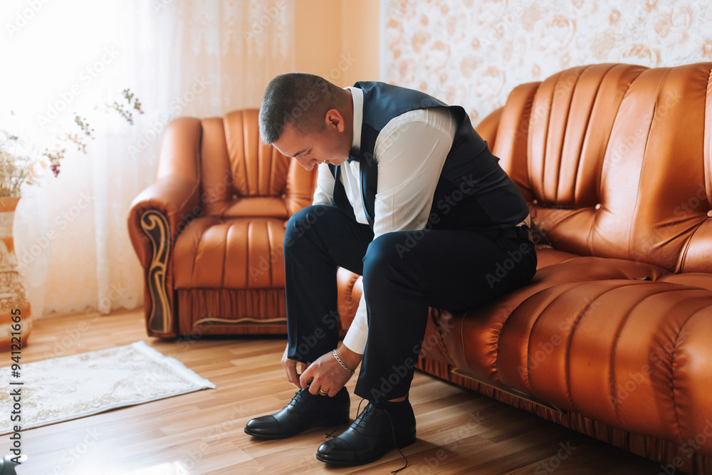 A man in a suit is sitting on a couch, fixing his shoes A man in a suit is sitting on a couch, fixing his shoes