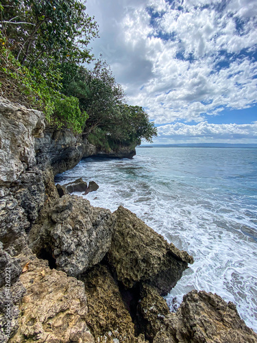 Hidden rocky beach with cliffs at Batukaras, Pangandaran, West Java, Indonesia during sunny day. Wavy beach with blue sky and clouds background. photo