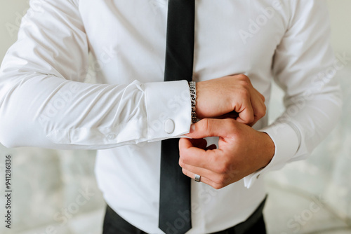 A man in a white shirt and black tie is adjusting his cuff. Concept of formality and attention to detail, as the man takes care to ensure his appearance is polished and professional