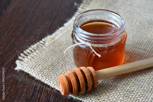 a jar of honey with a honeycomb next to it on burlap texture