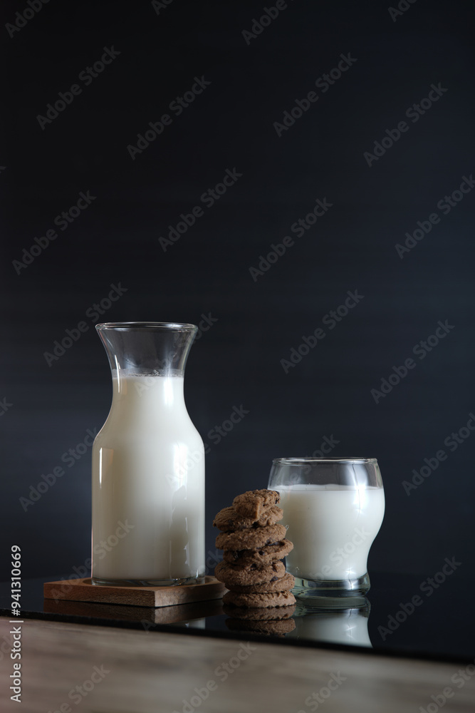 vertical view of a glass of milk and chocolatte cookies with reflective surface table and dark background vertical view of a glass of milk and chocolatte cookies with reflective surface table and dark background