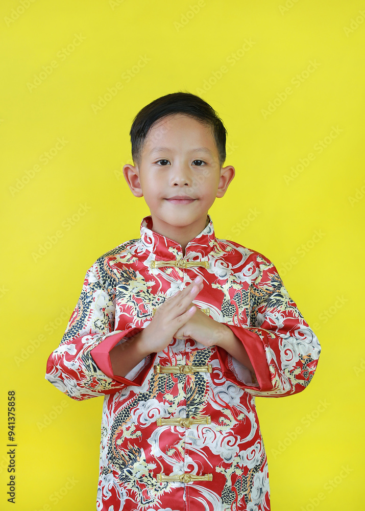 Happy Asian boy wearing cheongsam with greeting gesture celebration for Chinese New Year isolated on yellow background.