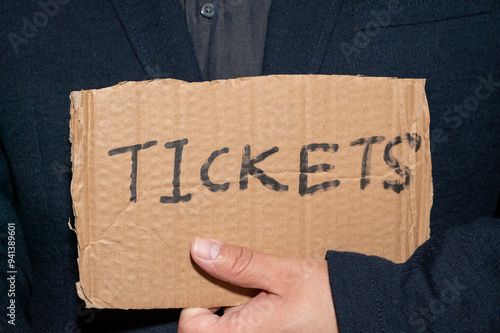 A man displays a sign advertising tickets for sale, a common practice among ticket scalpers
