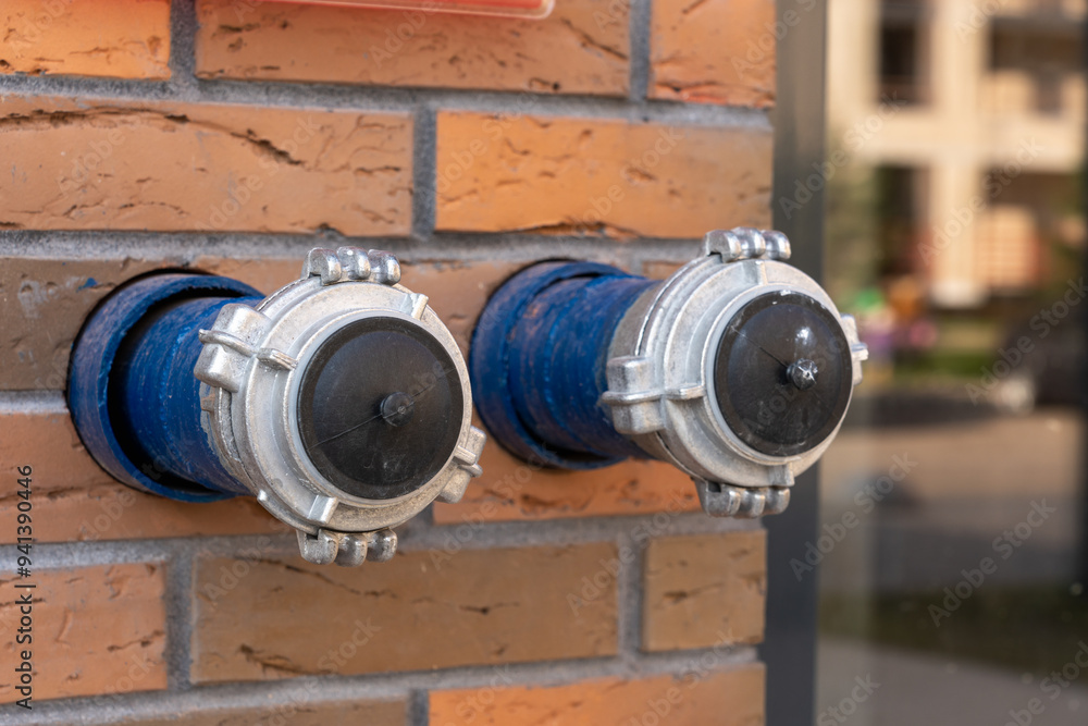 Two metal fire hydrant connections attached to a brick wall, ready for use in an emergency situation Two metal fire hydrant connections attached to a brick wall, ready for use in an emergency situation