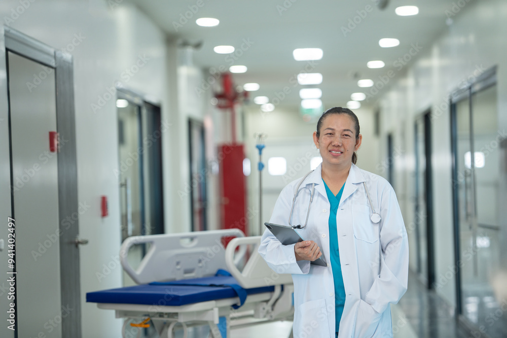 Naklejka premium A female doctor stands smiling, holding a tablet in her hand, preparing to work at the hospital