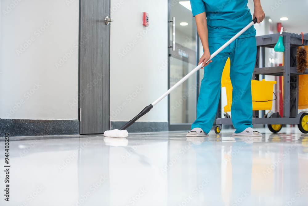 Fototapeta premium A mop operator in a blue uniform cleans new epoxy floor protection suits in an empty hospital warehouse.