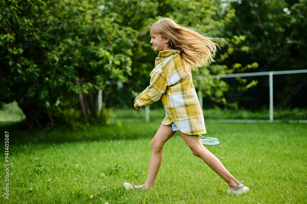 Teenage girl playing badminton on green grass in summer park