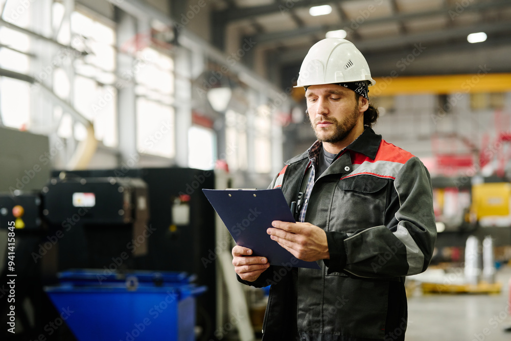 Portrait of engineer inspecting machinery in an industrial setting while holding clipboard Portrait of engineer inspecting machinery in an industrial setting while holding clipboard