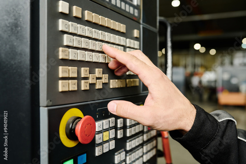 Close-up of a person's hand adjusting settings on an industrial control panel in a factory environment