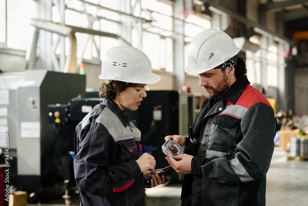 Two workers in an industrial workshop inspecting machinery with serious focus wearing protective gear Two workers in an industrial workshop inspecting machinery with serious focus wearing protective gear