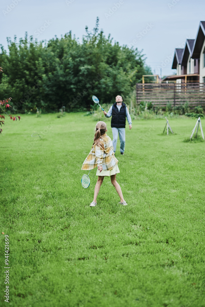 Fototapeta premium Teenage girl playing badminton with her father on green grass in summer park