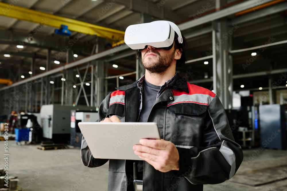 Adult male worker using virtual reality headset while holding digital tablet in hands Adult male worker using virtual reality headset while holding digital tablet in hands